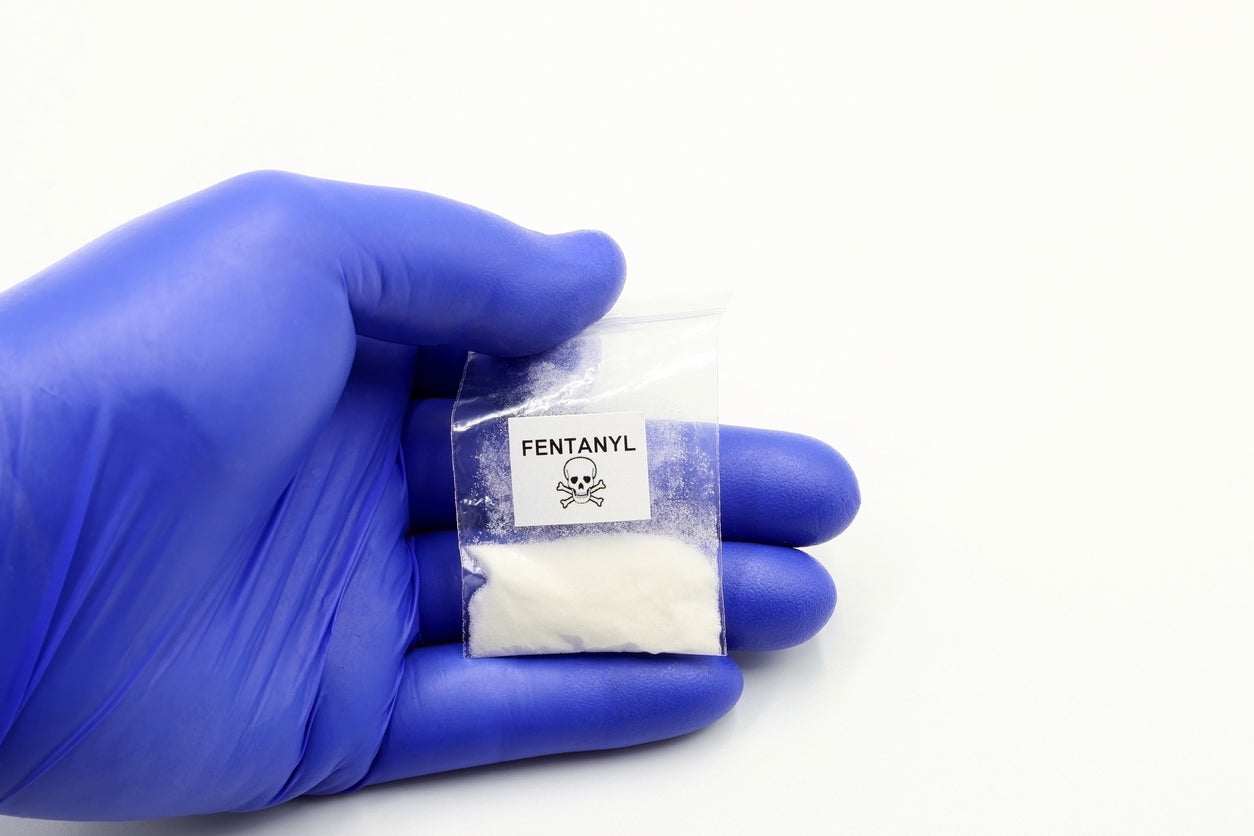 Hand in blue glove holding a bag labeled Fentanyl with a hazard symbol