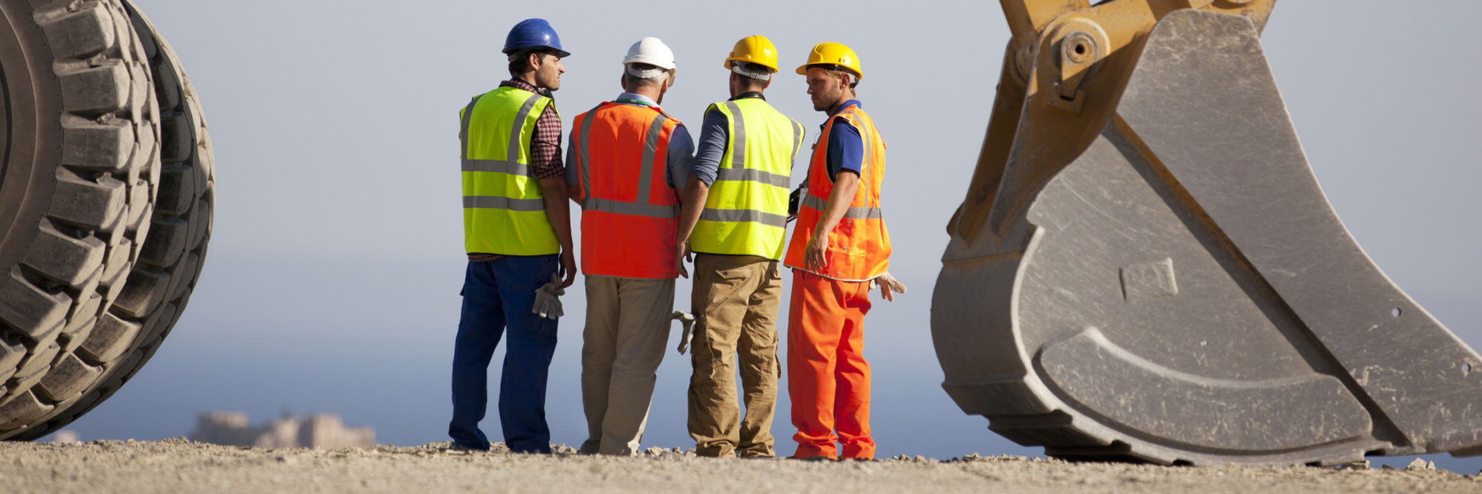 Four construction workers in safety gear having a discussion near large machinery
