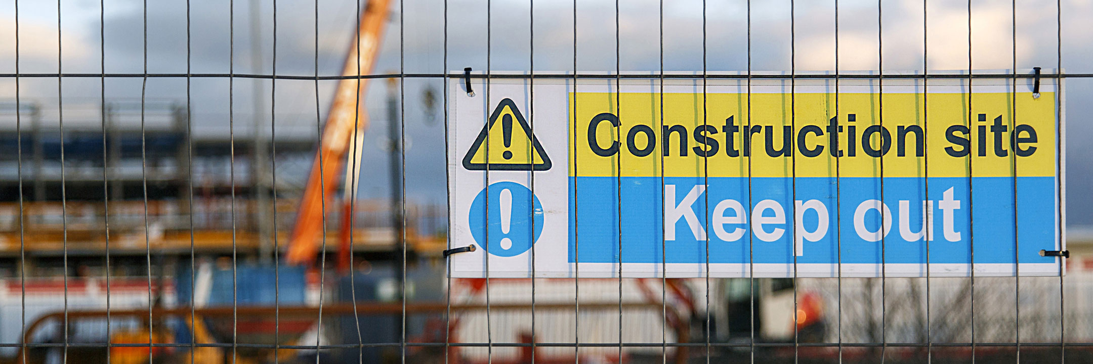 Warning sign on a fence at a construction site reads 'Construction site Keep out' with a caution symbol