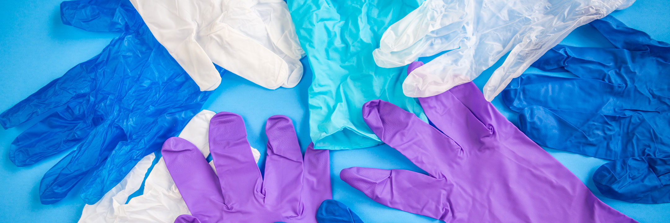 Assorted colored disposable gloves spread out on a blue surface